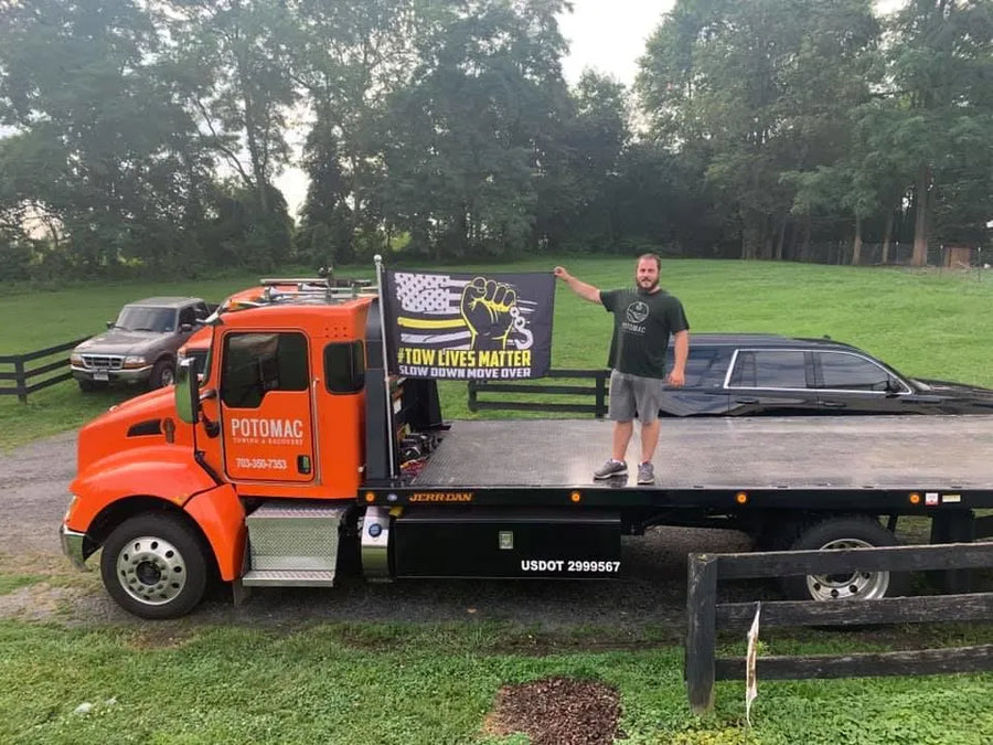 Tow operator standing on his flatbed tow truck holding a Tow Lives Matter Slow Down Move Over flag