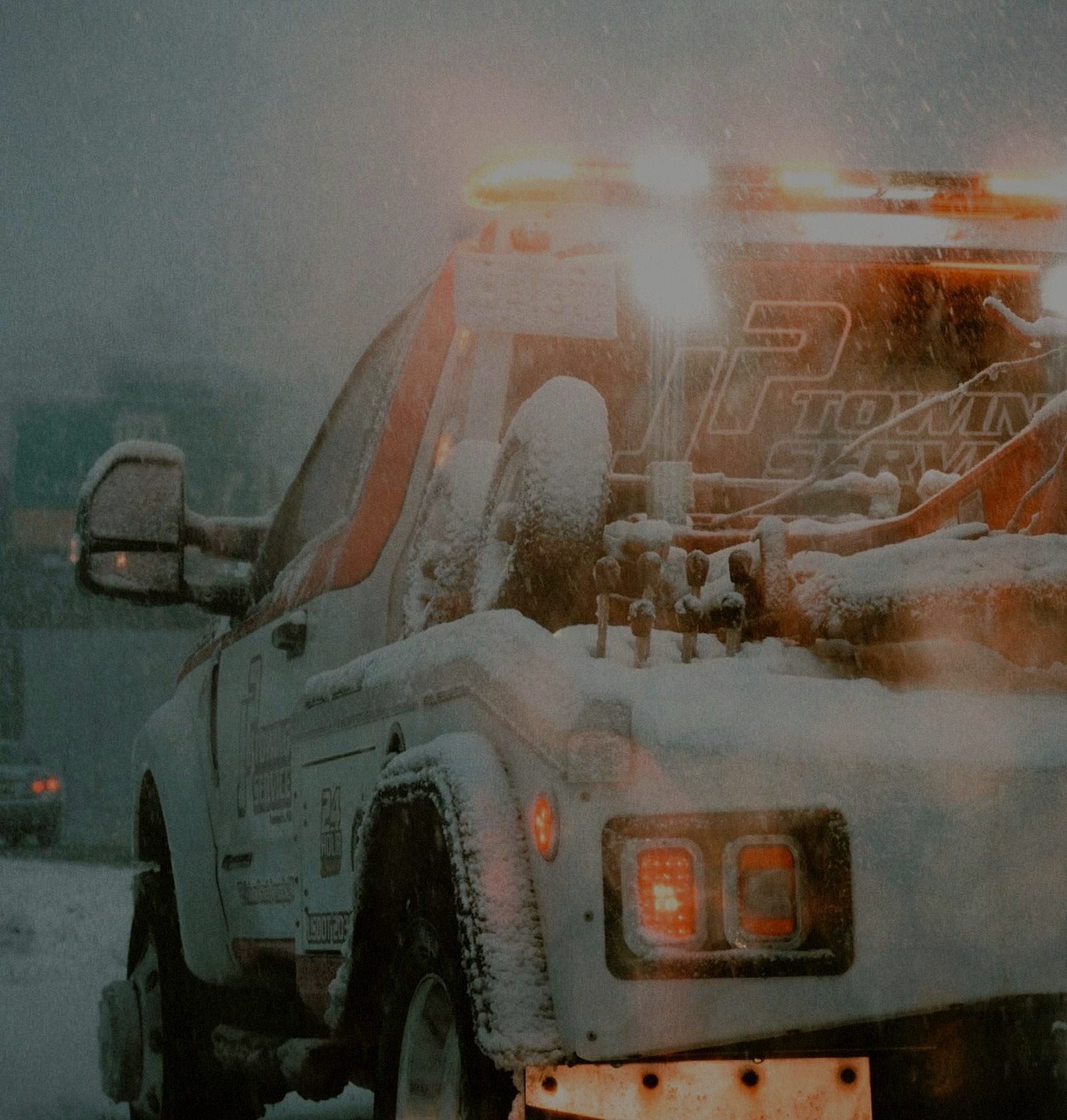 Tow truck with its amber light bar on, working through a snowstorm
