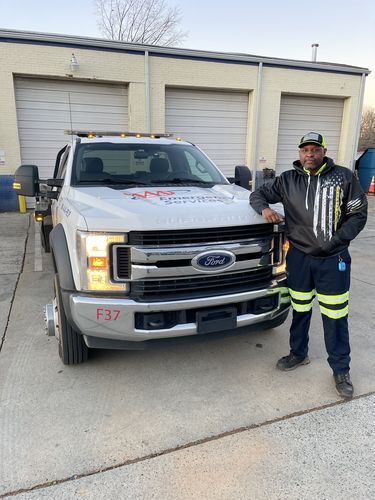 Tow operator in a black hoodie standing beside his white tow truck