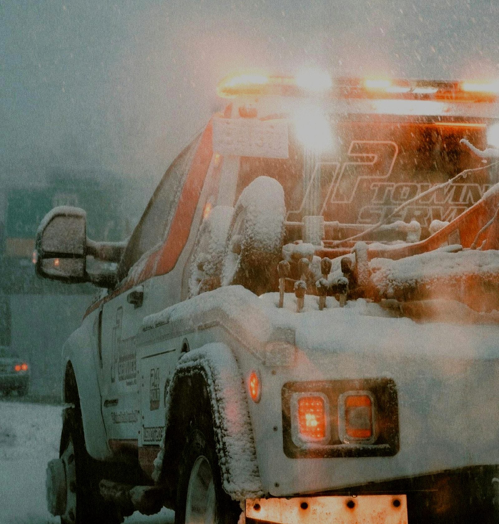 Tow truck with its amber light bar on, working through a snowstorm
