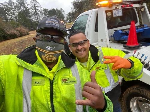 Two tow operators in high-visibility jackets beside their wrecker