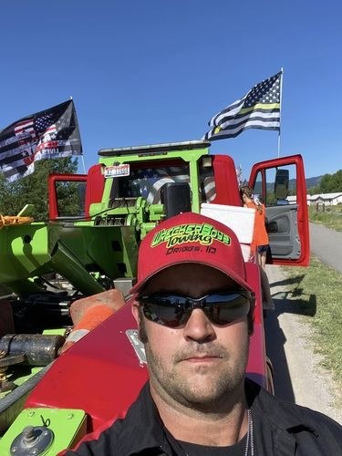 Tow operator in a red cap in front of his truck flying a thin yellow line flag