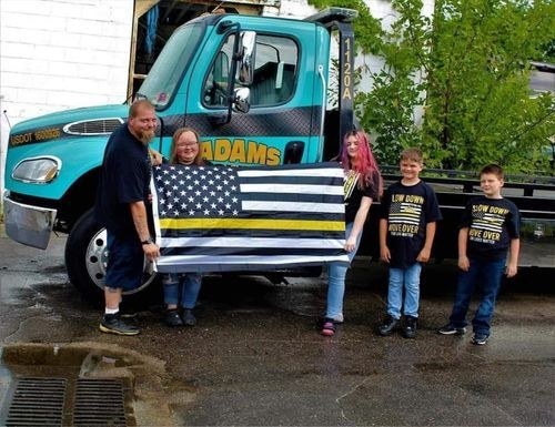 A tow family and their crew holding a thin yellow line flag in front of their tow truck